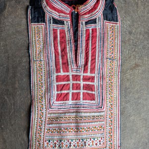 May include: A red and black embroidered vest with intricate geometric patterns. The vest has a V-neck and is made of a soft, textured fabric.