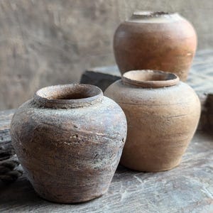 May include: Three brown clay pots of varying sizes and shapes. The pots are rustic and have a worn, aged appearance.