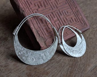 Könnte beinhalten: Ein Paar silberne Creolen mit aufwendigen Blumendesigns. Die Ohrringe sind aus dickem, schwerem Metall gefertigt und haben eine leicht gebogene Form.