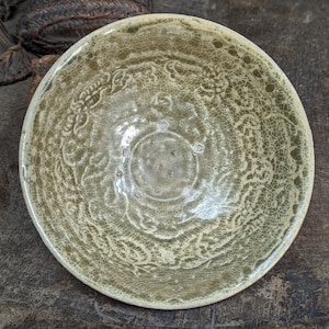 May include: A light green ceramic bowl with a crackled glaze and a decorative design. The bowl has a circular shape and a slightly raised rim.