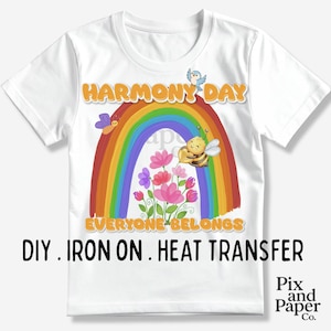 May include: White t-shirt with a rainbow design, a bee, flowers, and the text "HARMONY DAY" and "EVERYONE BELONGS". The shirt also has the text "DIY . IRON ON . HEAT TRANSFER".