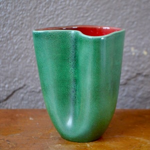 May include: A green ceramic vase with a red interior. The vase has a unique, asymmetrical shape and a textured surface.