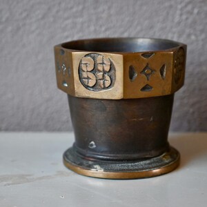 Peut inclure: Un petit mortier et pilon octogonal en bronze avec des motifs décoratifs sur le bord supérieur. Le mortier est brun foncé et le pilon est manquant.
