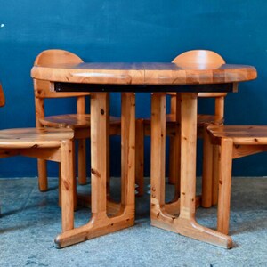 Peut inclure: Un ensemble de quatre chaises en bois et une table ronde en bois avec un plateau brun foncé. Les chaises et la table sont toutes en bois clair et ont un design simple et rustique.