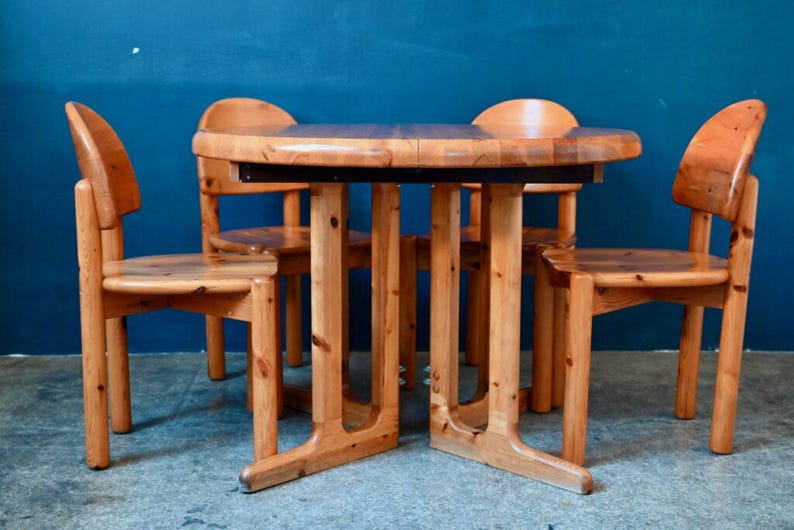 May include: A set of four wooden chairs and a round wooden table with a dark brown top. The chairs and table are all made of light wood and have a simple, rustic design.