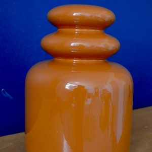 May include: A ceramic vase with a rounded, bulbous shape. The vase is a deep orange color and has a glossy finish.