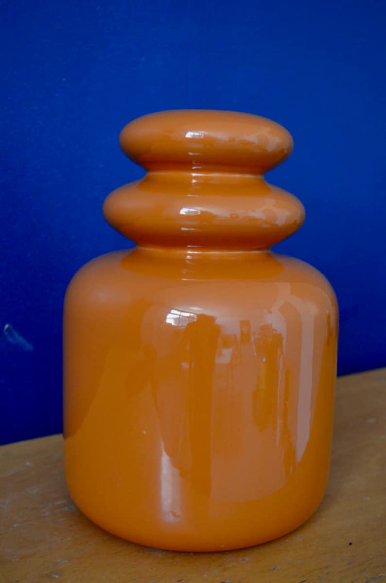 May include: A ceramic vase with a rounded, bulbous shape. The vase is a deep orange color and has a glossy finish.