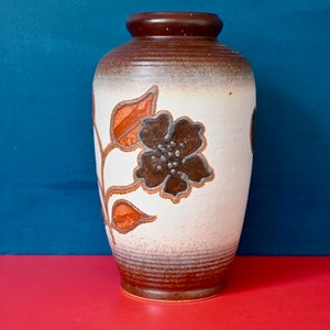 Peut inclure: Un vase en céramique brun et blanc avec un motif floral. Le vase est recouvert d'un glacis brun avec une bande blanche autour du milieu. Le motif floral est dans des tons de brun, orange et blanc.