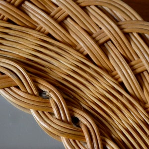 May include: Close-up of a woven wicker frame, showing the intricate details of the natural material. The frame is made of light brown, tightly woven strands of wicker, creating a textured and organic pattern.