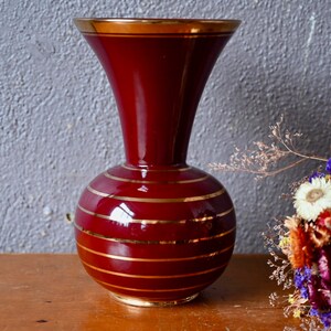 May include: A red ceramic vase with gold stripes. The vase has a round base and a narrow neck.