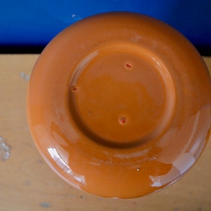 May include: The bottom of a terracotta-colored ceramic pot. The pot has a smooth, glazed finish and a circular base.