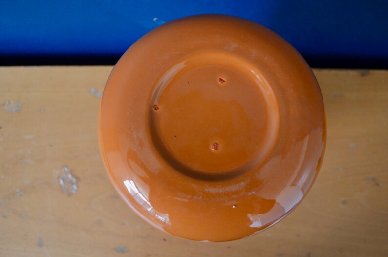 May include: The bottom of a terracotta-colored ceramic pot. The pot has a smooth, glazed finish and a circular base.