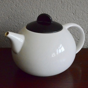 May include: White ceramic teapot with a black lid and a round body. The teapot has a spout and a handle.