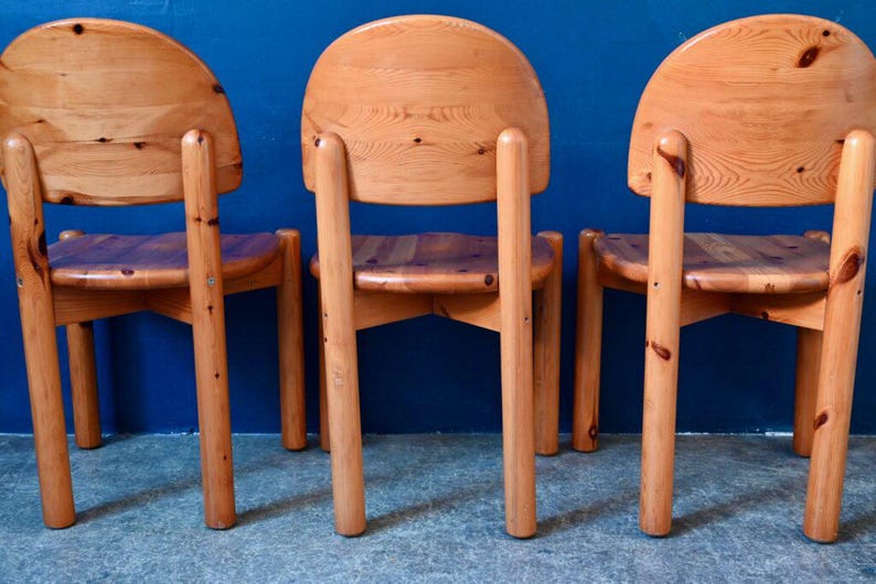 May include: Three wooden chairs with a light brown finish. The chairs have a rounded back and four legs. The chairs are arranged in a row.