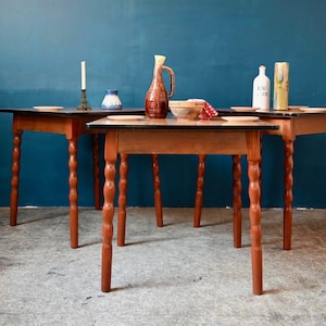 Peut inclure: Trois tables en bois avec des plateaux sombres et des pieds tournés sont disposées dans une pièce avec un mur bleu canard. Les tables sont ornées de divers objets décoratifs, dont une bougie, un vase, une cruche et un bol.