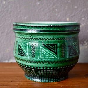 Peut inclure: Un cache-pot en céramique verte orné d'un motif géométrique vert foncé et noir sur l'extérieur. Le design comprend des lignes en zigzag horizontales, des motifs en forme de feuilles et un quadrillage près de la base. L'intérieur est blanc.