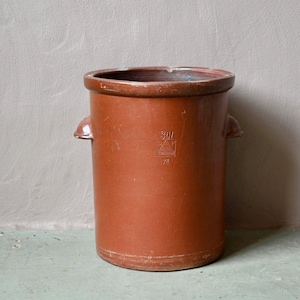 May include: A cylindrical brown stoneware crock featuring two small side handles and a stamped logo on the front. The vessel has a smooth, matte finish with a wide opening at the top and a sturdy base, showing a distinct embossed mark with the text 3W.