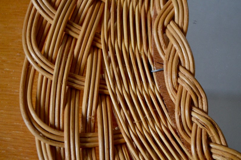 May include: Close-up of a woven wicker frame with a natural brown color. The frame is made of thin, tightly woven strips of wicker, creating a detailed and intricate pattern.