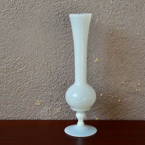 Könnte beinhalten: Eine weiße Glas-Blumenvase mit rundem Korpus und einem ausgestellten Fuß. Die Vase hat eine strukturierte, matte Oberfläche.