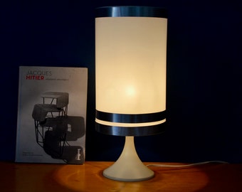 May include: A white table lamp with a frosted glass shade and a silver band around the middle. The lamp is on a wooden surface and is lit.