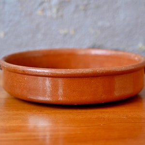 Puede incluir: Un plato de servir de terracota con dos asas. El plato es redondo y tiene un borde ligeramente elevado.