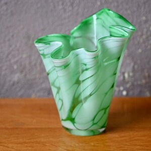 Peut inclure: Un vase en verre vert et blanc avec un design ondulé et plissé. Le vase est en verre transparent avec des tourbillons verts et blancs.