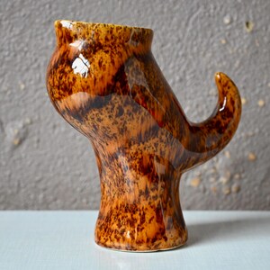 以下が含まれることがあります： ユニークな抽象的な形をした茶色とオレンジ色のセラミックの花瓶。光沢のある仕上げと渦巻き模様が施されています。