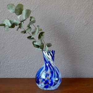 Peut inclure: Un vase en verre bleu et blanc avec un motif en spirale. Le vase est rempli de feuilles d'eucalyptus séchées.