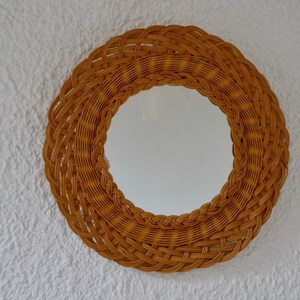 May include: A round mirror with a woven wicker frame. The frame is a light brown color and has a natural, rustic look.