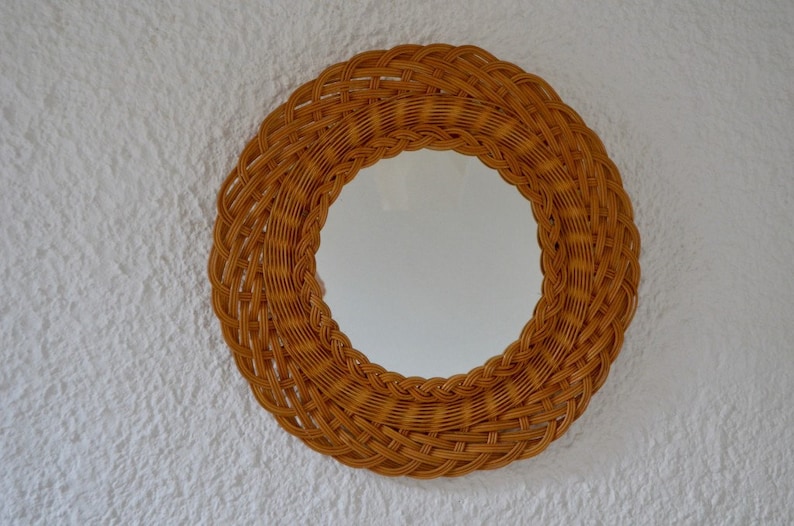 May include: A round mirror with a woven wicker frame. The frame is a light brown color and has a natural, rustic look.