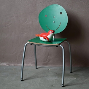 Peut inclure: Une chaise verte avec un visage souriant sur le dossier. La chaise a un cadre en métal argenté et un siège vert. Un jouet phoque rouge et blanc est assis sur le siège.