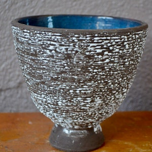 Peut inclure: Un vase en céramique brun avec un glaçage blanc et un intérieur bleu. Le vase a une surface texturée et une base large.