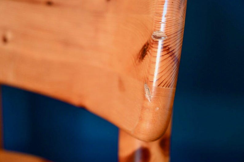 May include: Close-up of the back of a wooden chair with a natural wood finish. The chair has a curved back and a smooth, polished surface.