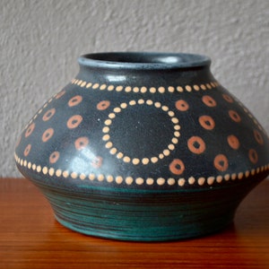 May include: A dark blue ceramic vase with a geometric pattern of orange and white circles. The vase has a wide base and a narrow opening.