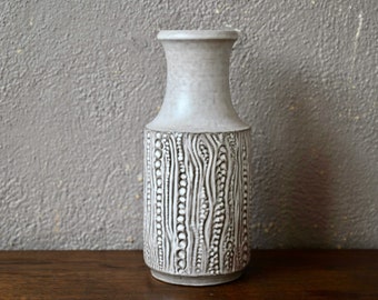 May include: A white ceramic vase with a textured design of raised dots and lines. The vase has a narrow neck and a wide base.