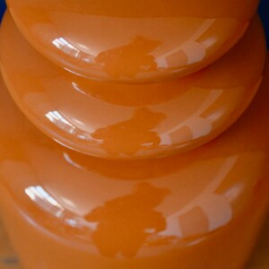 May include: A stack of three orange ceramic bowls with a glossy finish. The bowls are stacked in a graduated size, with the largest bowl at the bottom and the smallest bowl at the top. The bowls are all round and have a smooth, even surface.