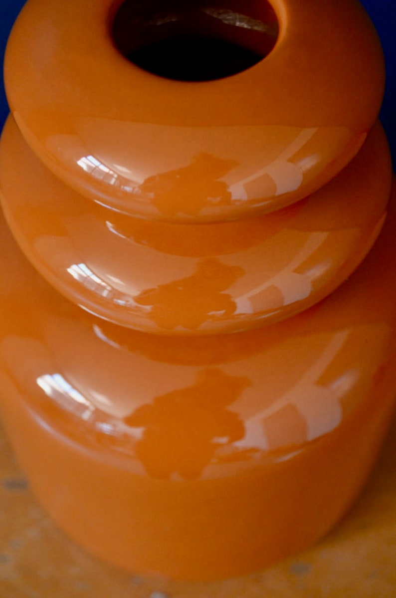 May include: A stack of three orange ceramic bowls with a glossy finish. The bowls are stacked in a graduated size, with the largest bowl at the bottom and the smallest bowl at the top. The bowls are all round and have a smooth, even surface.