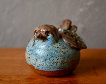 Op de afbeelding: Een blauwe en bruine keramische vogelfiguur met gespikkelde glazuur. De vogel heeft een rond lichaam en een kleine snavel.