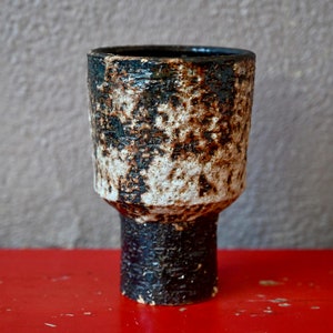 Peut inclure: Un vase en céramique avec un glaçage moucheté blanc et noir. Le vase a un haut cylindrique large et une base cylindrique étroite.