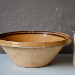 Puede incluir: Un tazón grande de cerámica de color crema con rayas marrones alrededor del borde. El tazón está ligeramente astillado en el borde.