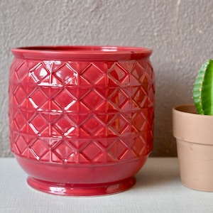 Op de afbeelding: Een rode keramische plantenpot met een ruitpatroon. De pot is leeg en staat op een wit oppervlak.