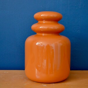 May include: A bright orange ceramic vase with a unique, rounded, layered design. The vase has a glossy finish and is perfect for adding a modern touch to any home decor.