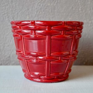 May include: A red ceramic planter with a woven design. The planter is glossy and has a rounded shape.