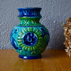 Peut inclure: Un vase en céramique bleu et vert avec un motif floral. Le vase a un corps rond et un col étroit.