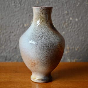 May include: A white ceramic vase with a brown glaze. The vase has a round body and a narrow neck.