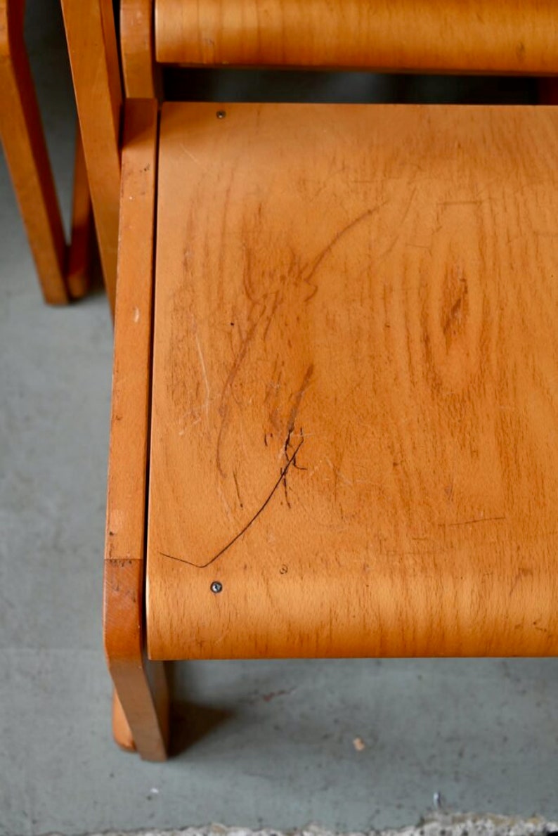 May include: A close-up of the wooden seat of a chair. The seat is made of light wood and has a few scratches on it.