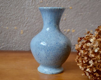 May include: A small, light blue ceramic vase with a speckled glaze. The vase has a round body and a narrow neck.