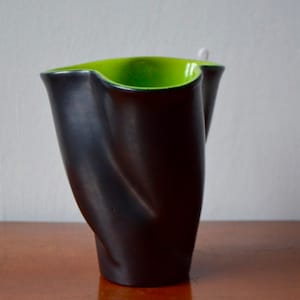 May include: A black ceramic vase with a green glazed rim. The vase has a unique, organic shape.
