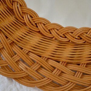 May include: Close-up of a woven wicker mirror frame. The frame is made of natural brown wicker and has a braided design around the edge.