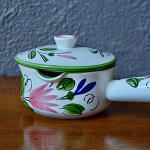 May include: White ceramic pot with a lid and a handle. The pot is decorated with green leaves, pink flowers, and blue accents.